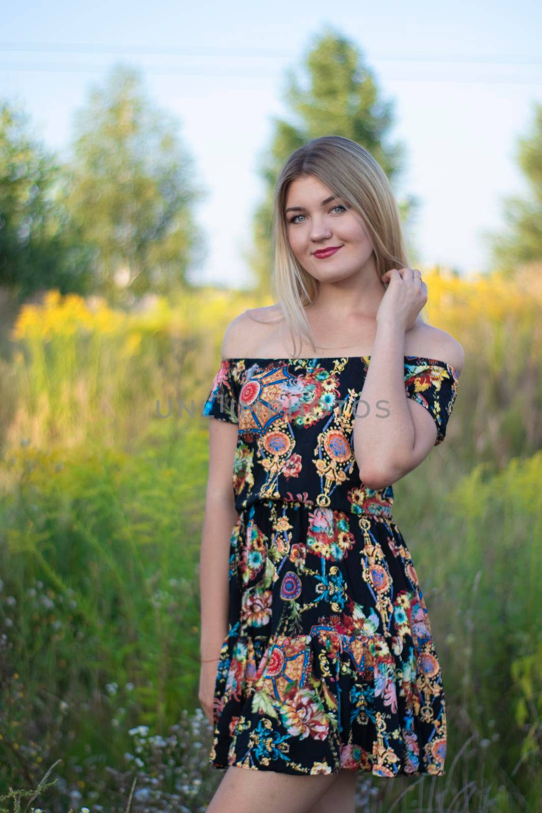 overlight bright portrait of a charming attractive blonde in flowery dress in the field.