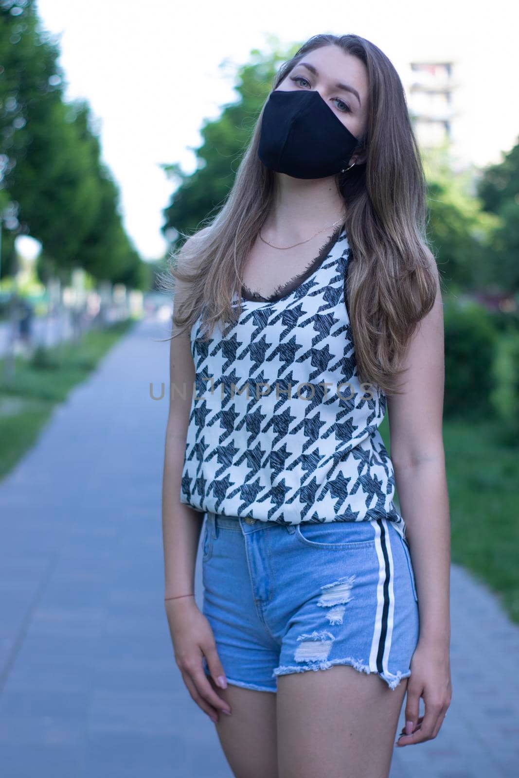 young blonde woman in medical black face mask. Wearing a t-shirt and jeans shorts. modern reality. covid-19 concept by oliavesna