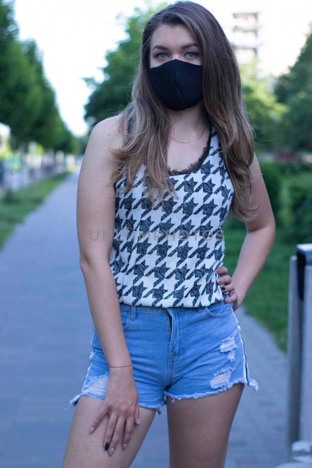 young blonde woman in medical black face mask. Wearing a t-shirt and jeans shorts. modern reality. covid-19 concept by oliavesna