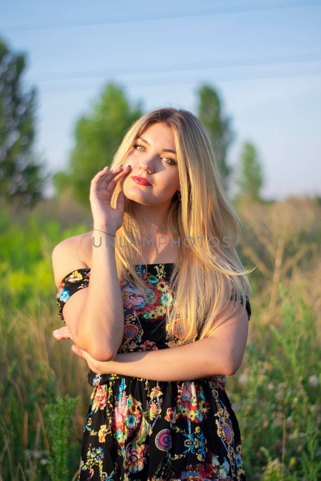 overlight bright portrait of a charming attractive blonde in flowery dress in the field.