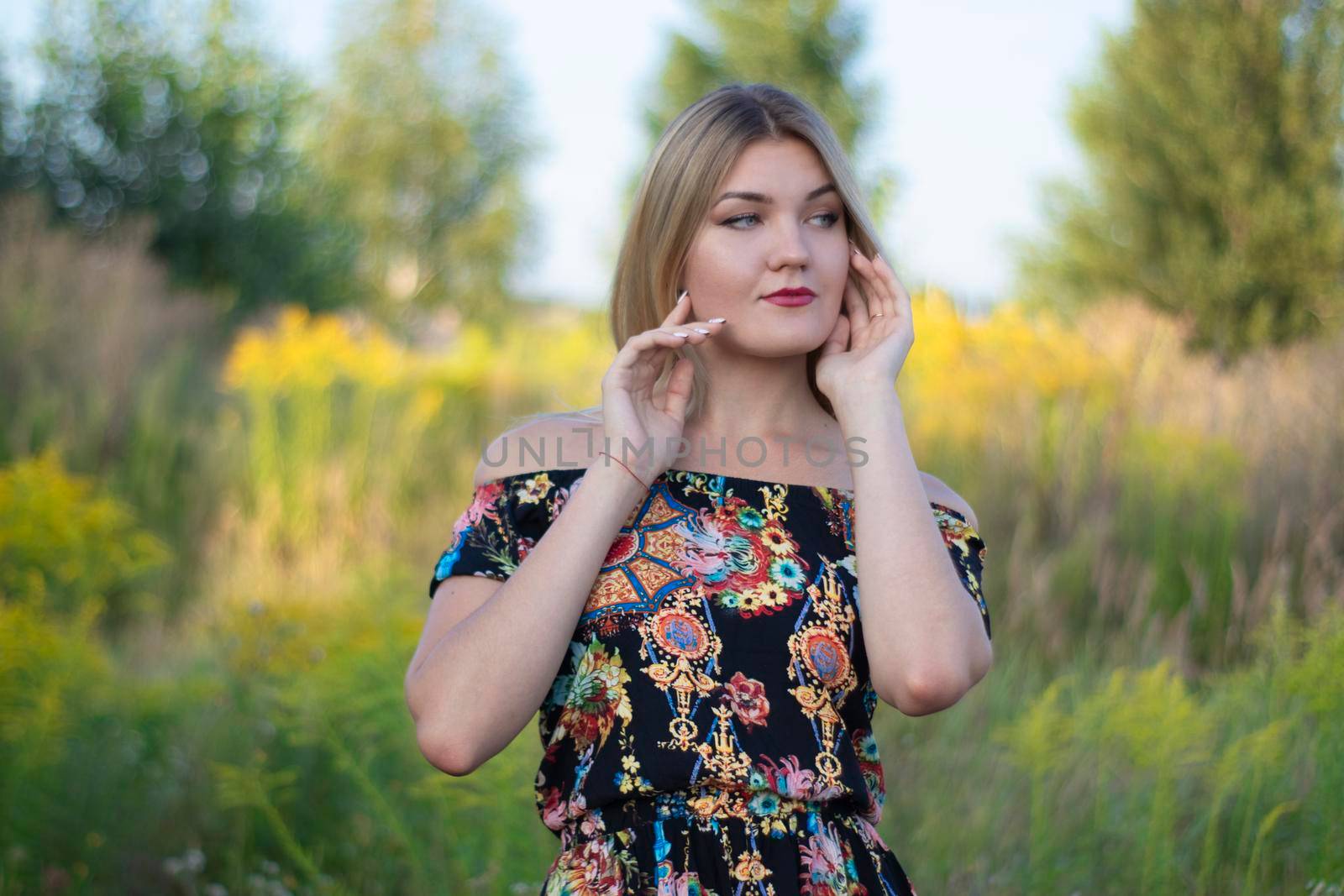 overlight bright portrait of a charming attractive blonde in flowery dress in the field.