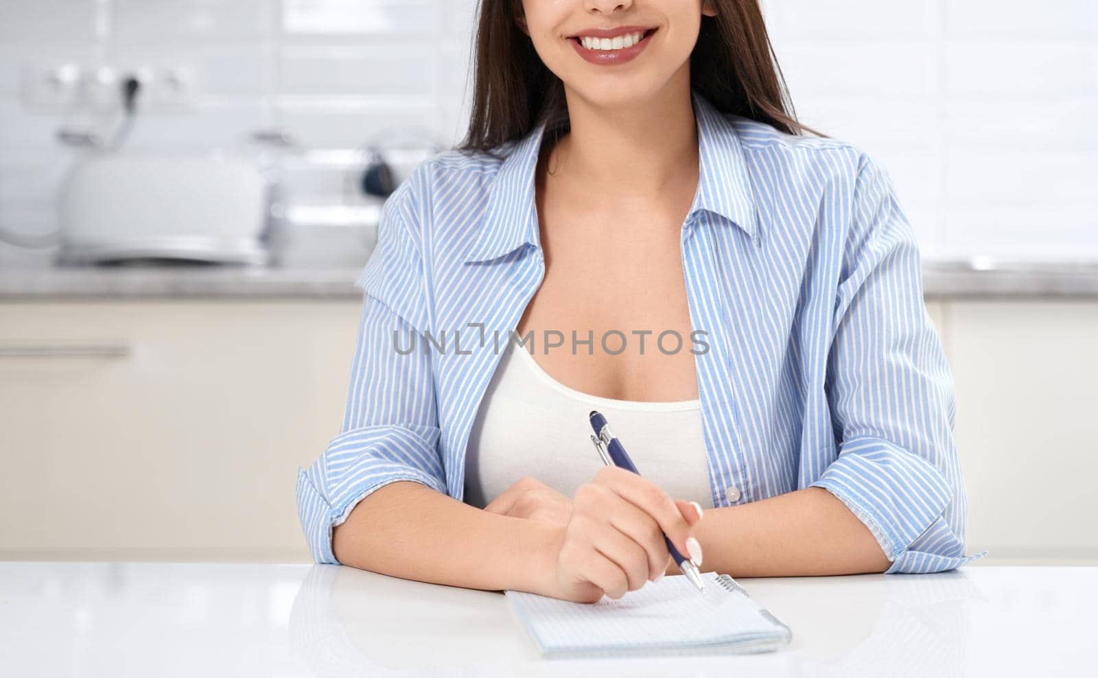 Close up of smiling woman sitting with notebook in kitchen. Concept of studying in quarantine.