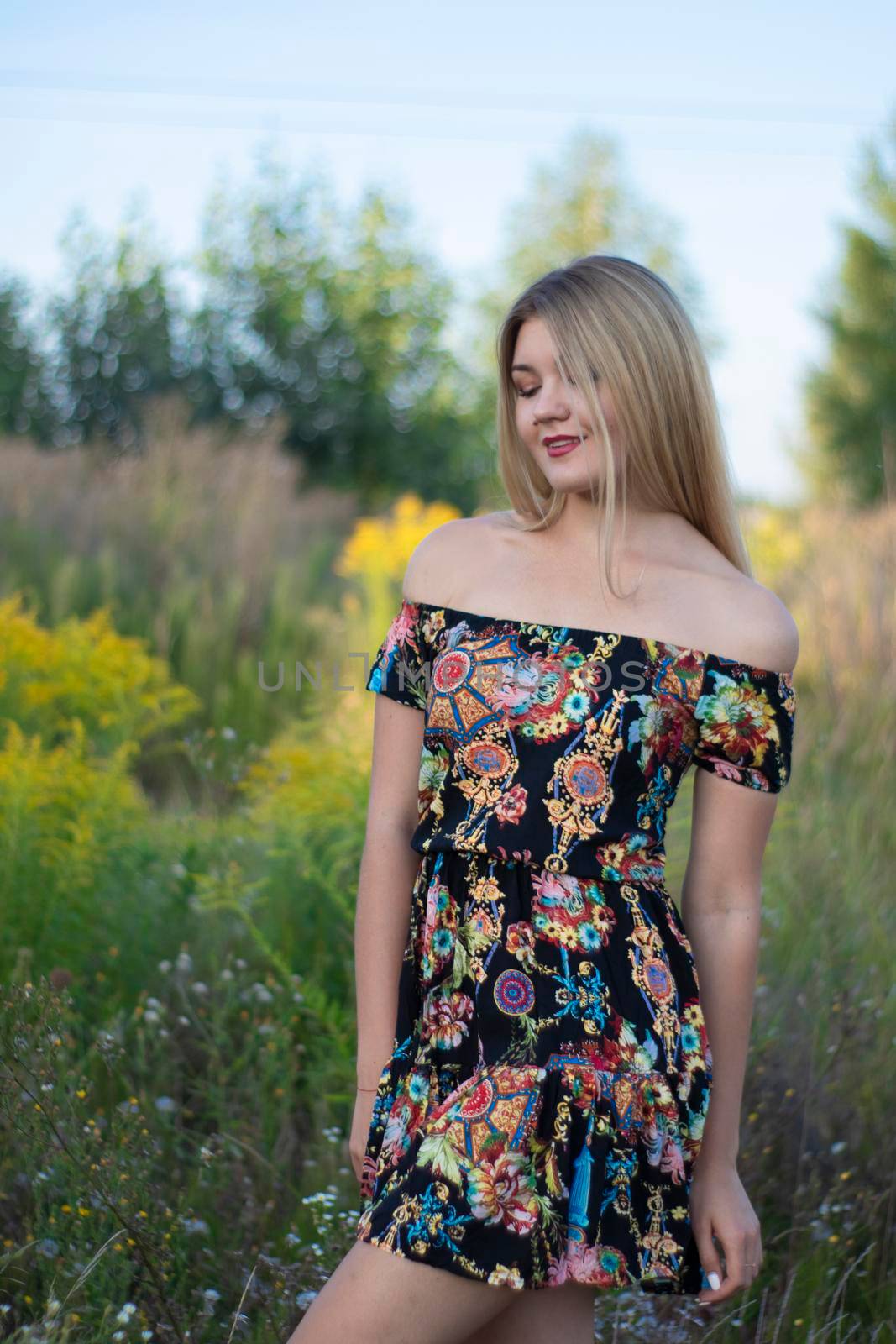 overlight bright portrait of a charming attractive blonde in flowery dress in the field.