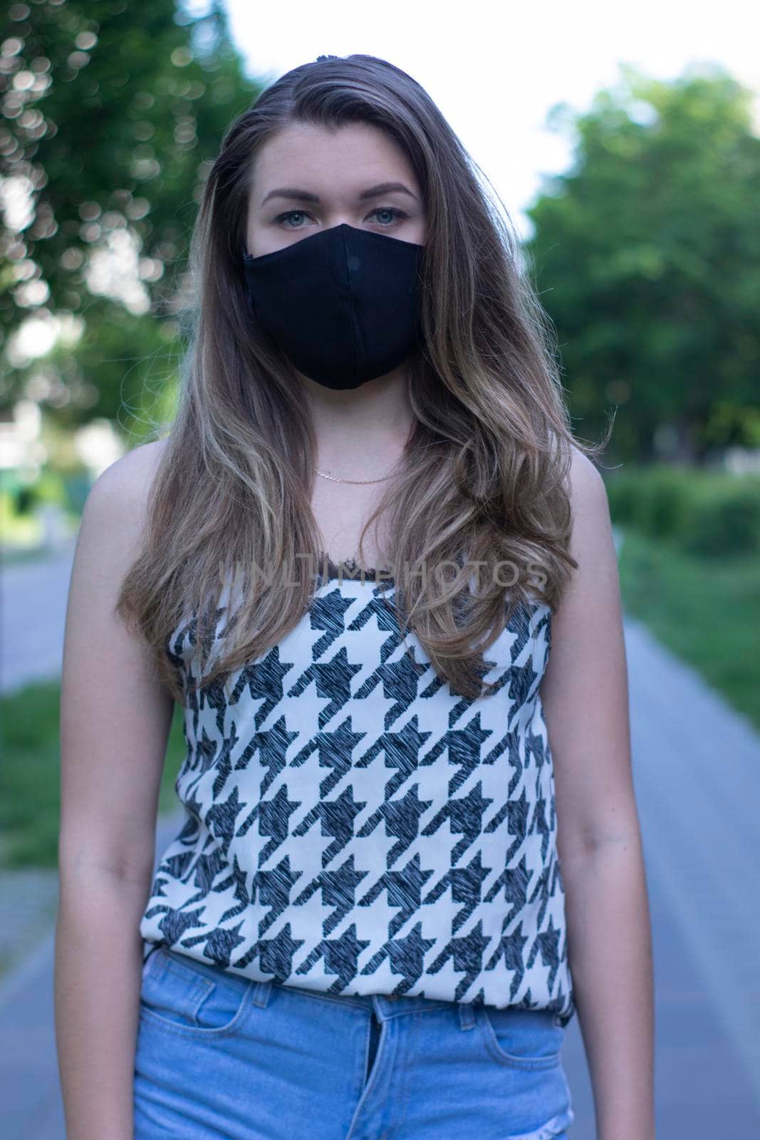 young blonde woman in medical black face mask. Wearing a t-shirt and jeans shorts. modern reality. covid-19 concept by oliavesna