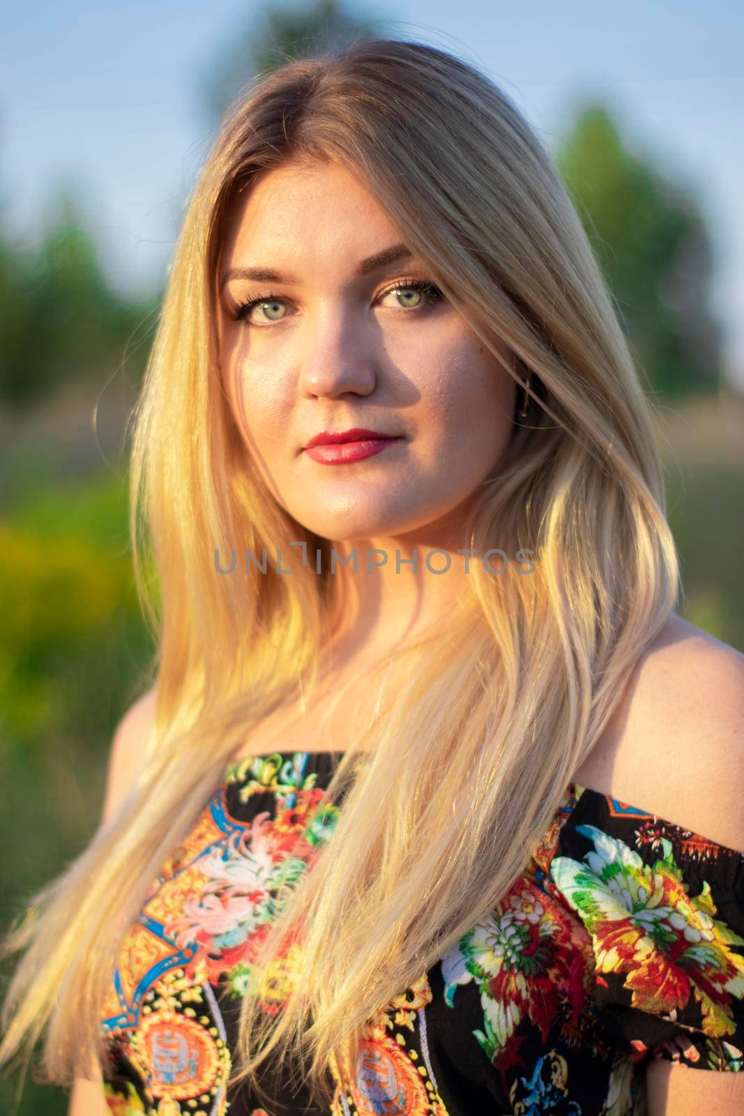 overlight bright portrait of a charming attractive blonde in flowery dress in the field.