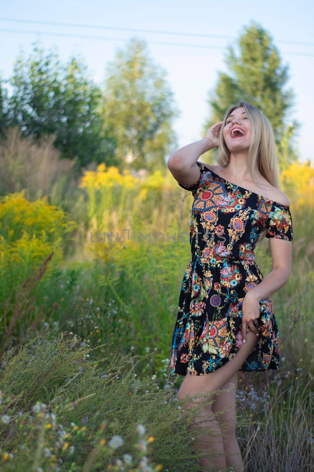 overlight bright portrait of a charming attractive blonde in flowery dress in the field.