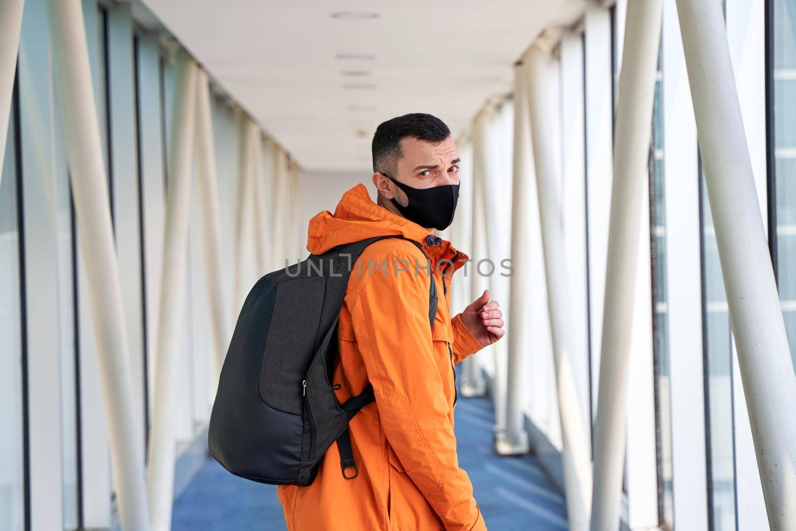 Guy tourist with a backpack and in a medical mask is walking along the airbridge from the plane to the airport terminal.