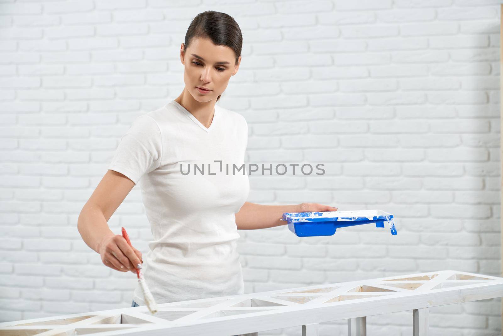 Cute woman holding white paint and painting wooden rack. by SerhiiBobyk