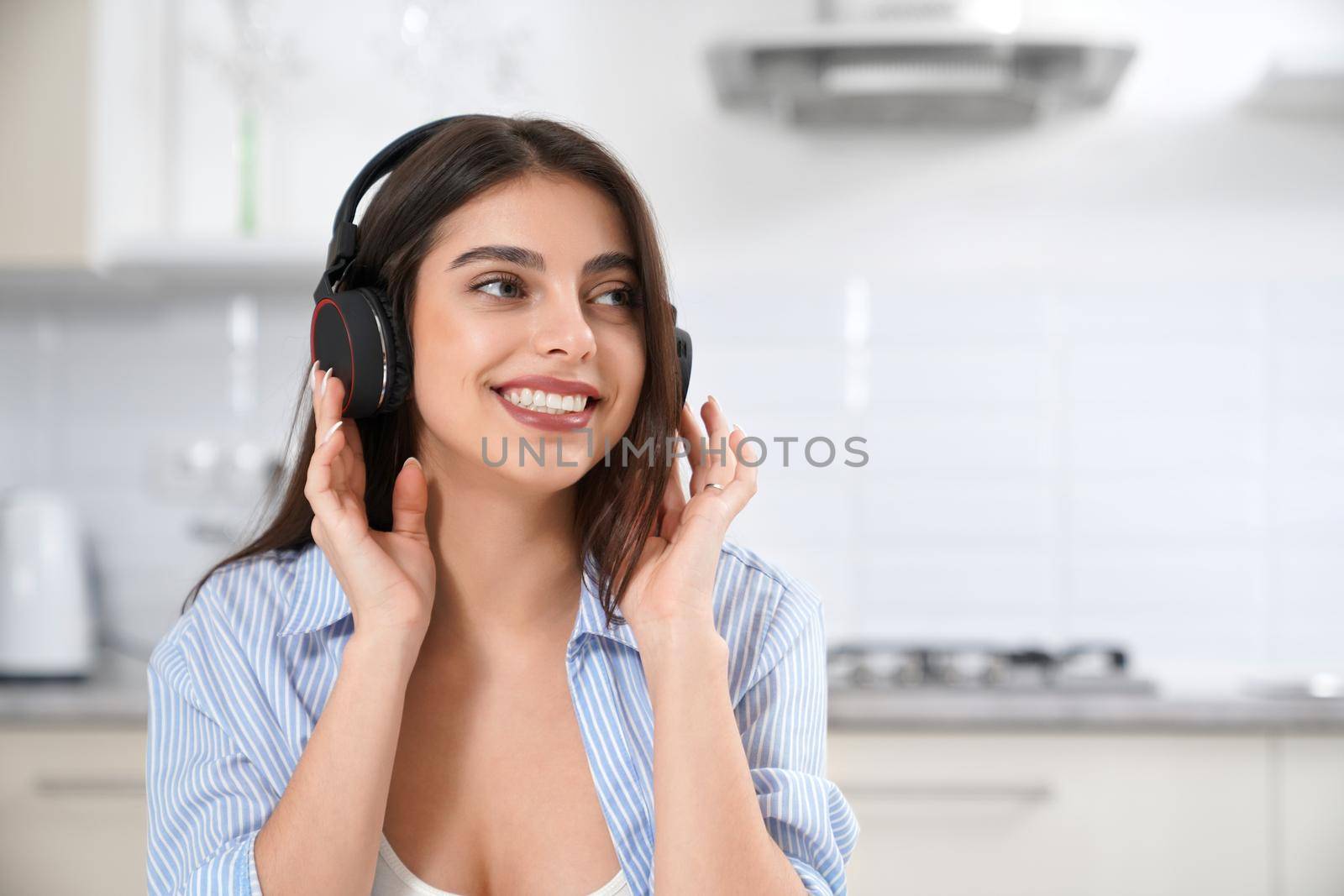 Close up of happy woman smiling and listening music in headphone at home in kitchen. Concept of leisure time at home.