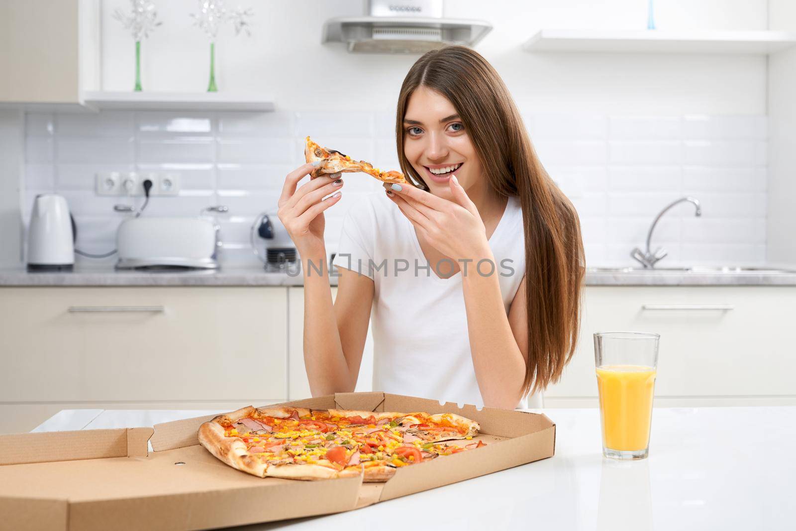Beautiful young woman eating delicious pizza on kitchen background. Concept of enjoying free time at home.