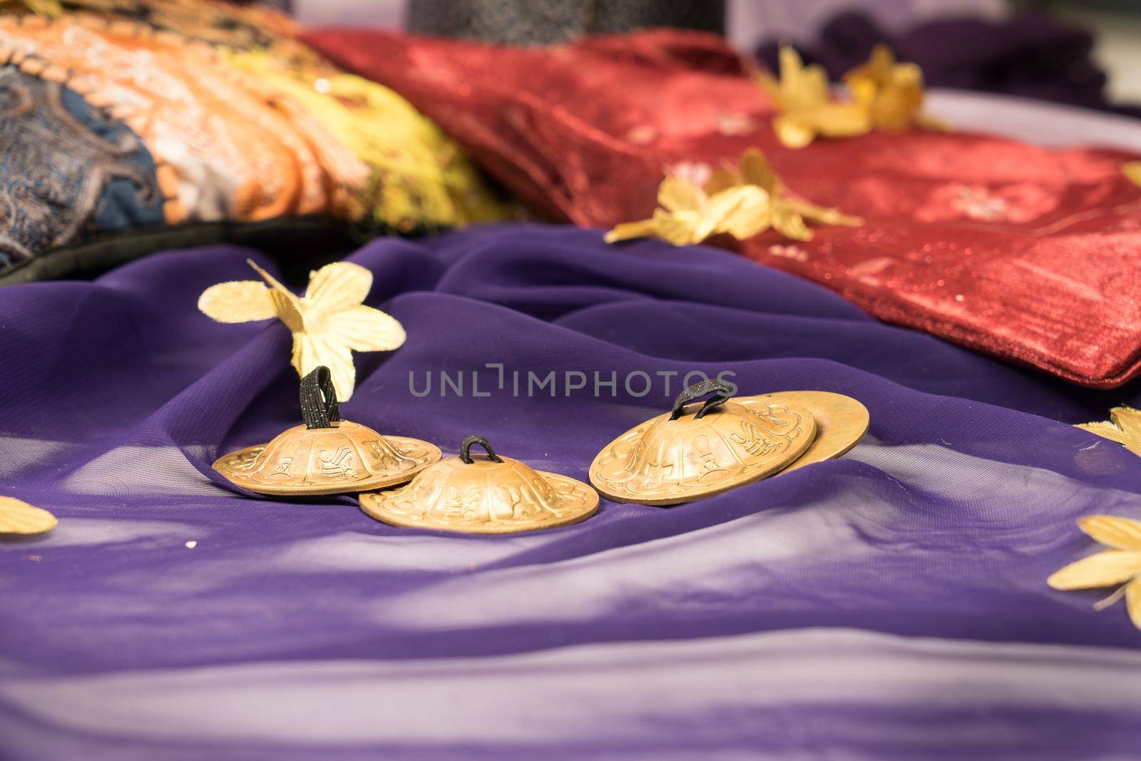 Close-up of zills for bellydancing on a purple veil with arabic cushions  by LeoniekvanderVliet