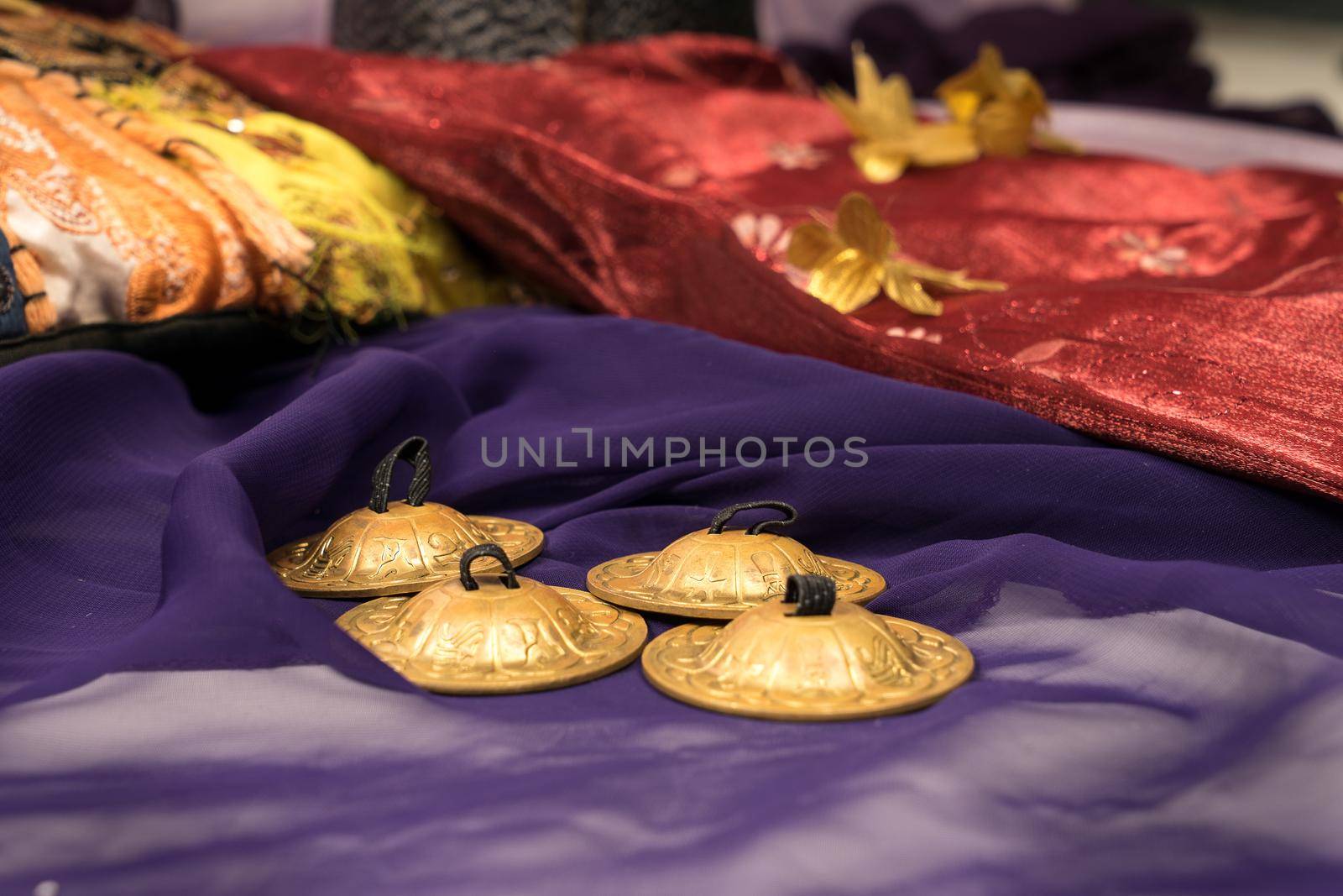 Close-up of zills for bellydancing on a purple veil with arabic cushions  by LeoniekvanderVliet