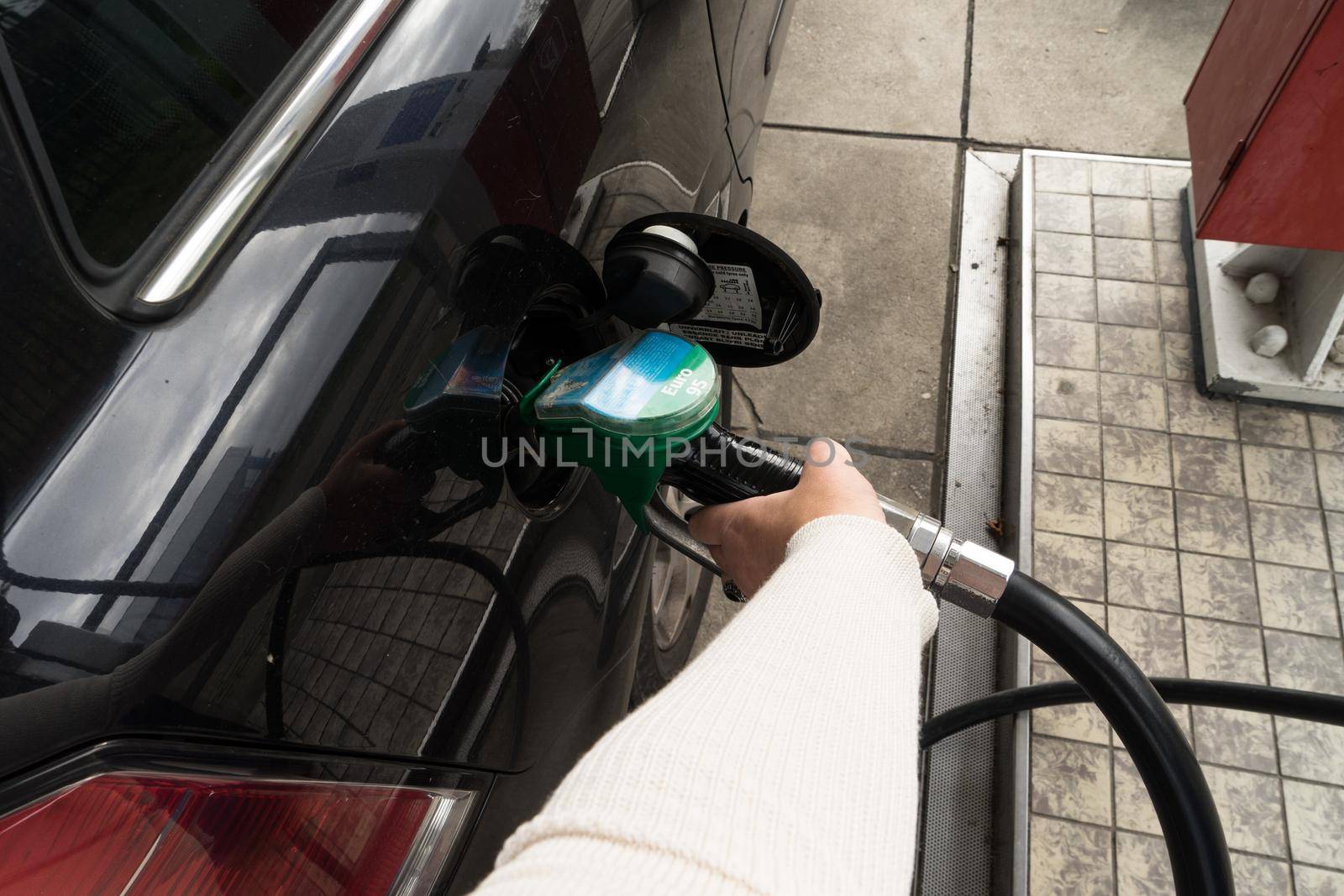 Female hand fill gasoline in a car with gas pump nozzle by LeoniekvanderVliet