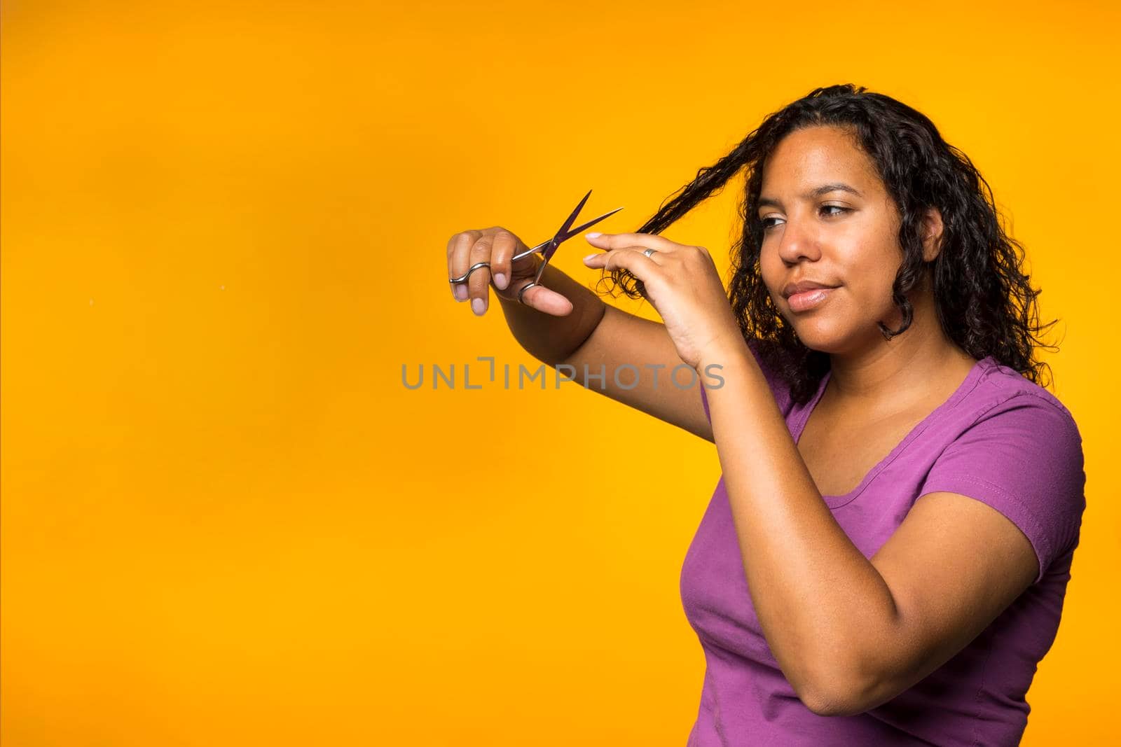 Young attractive mixed race woman cutting her hair in a yellow background