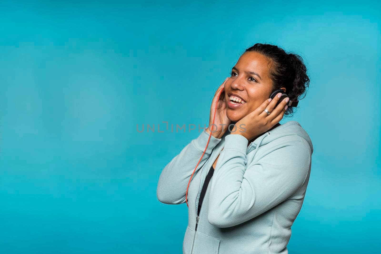 Young attractive mixed race woman enjoying music listening with headphones blue background by LeoniekvanderVliet