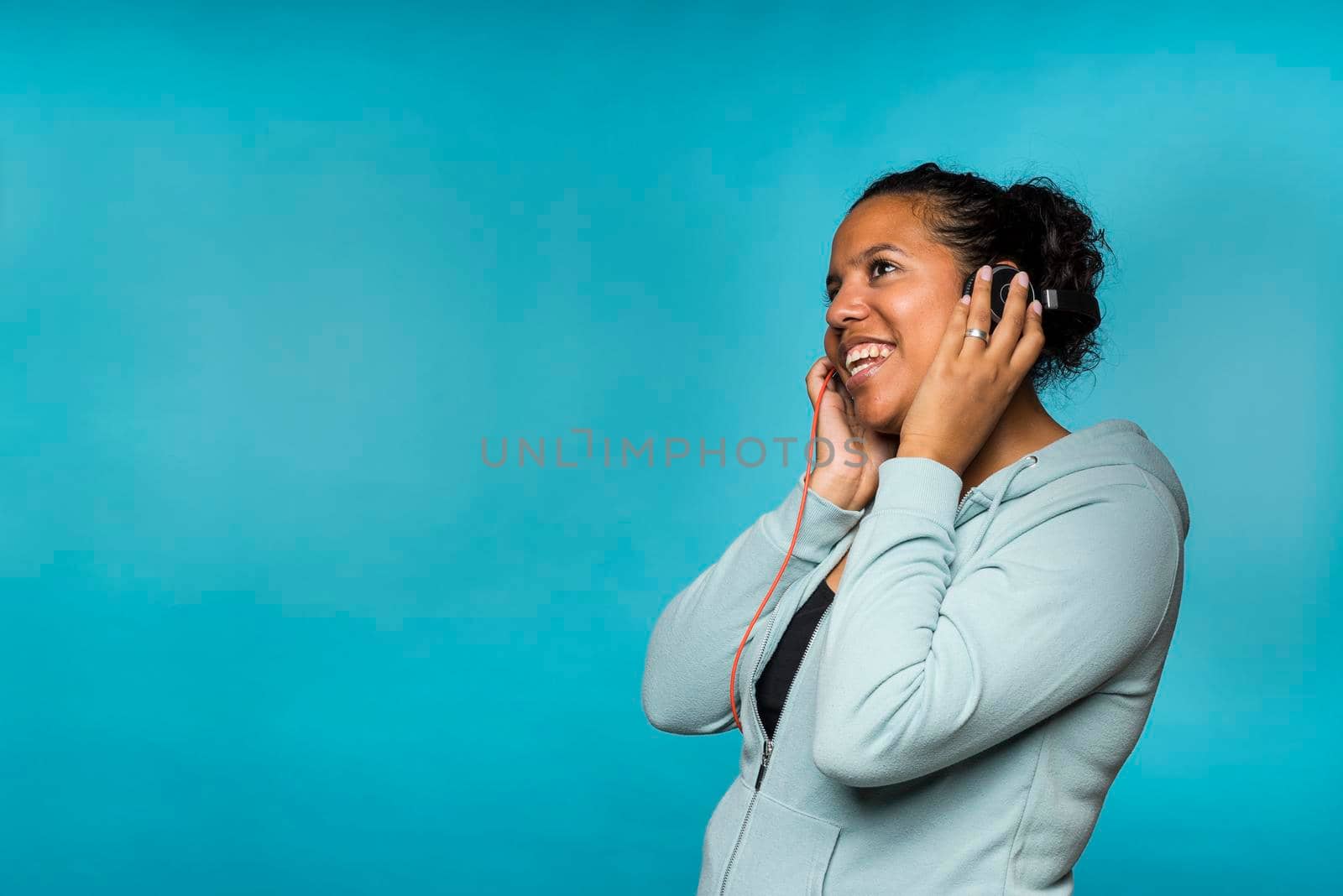 Young attractive mixed race woman enjoying music listening with headphones blue background