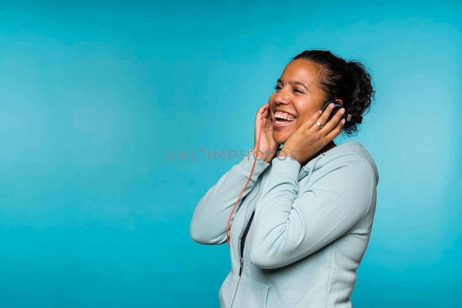 Young attractive mixed race woman enjoying music listening with headphones blue background by LeoniekvanderVliet