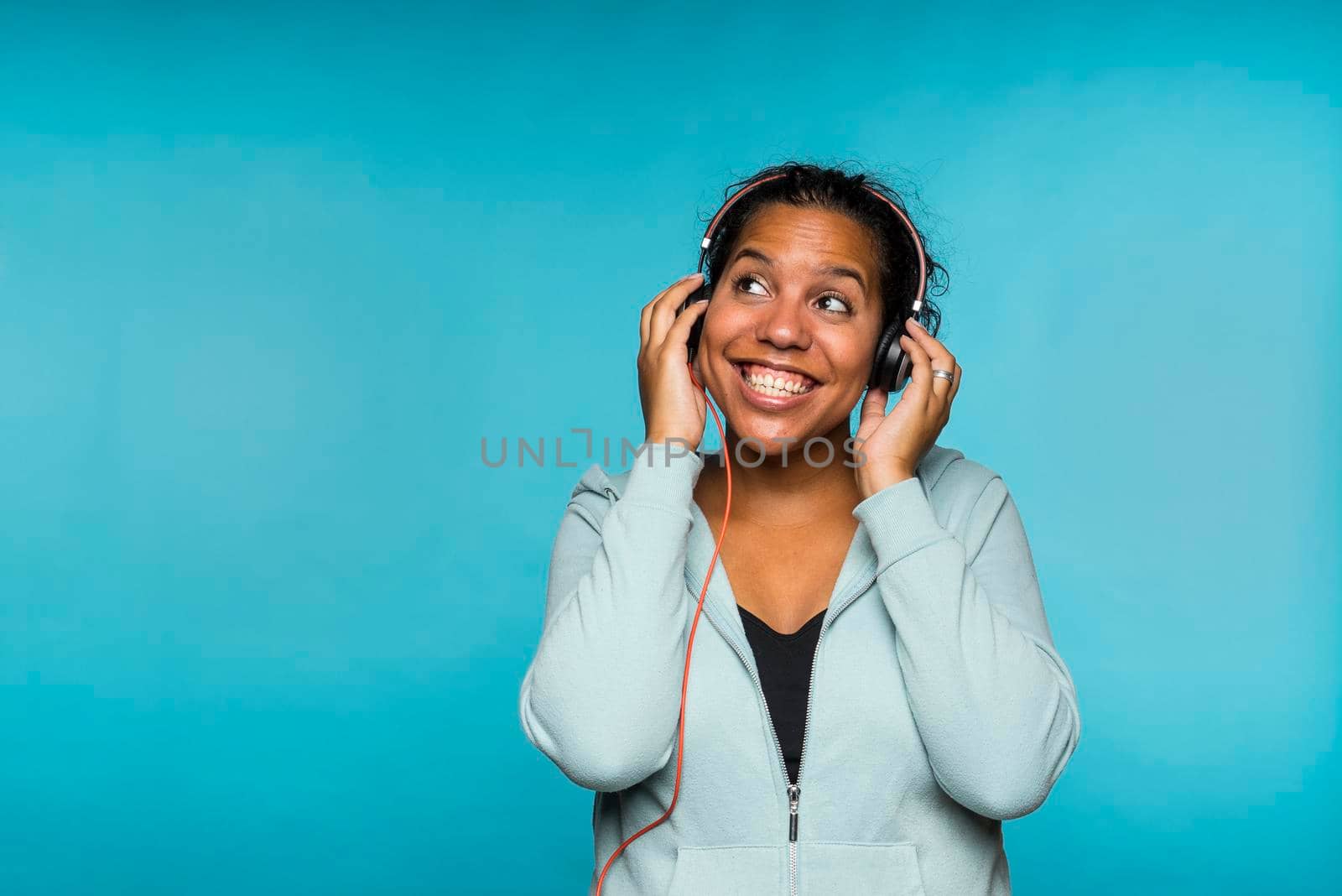 Young attractive mixed race woman enjoying music listening with headphones blue background