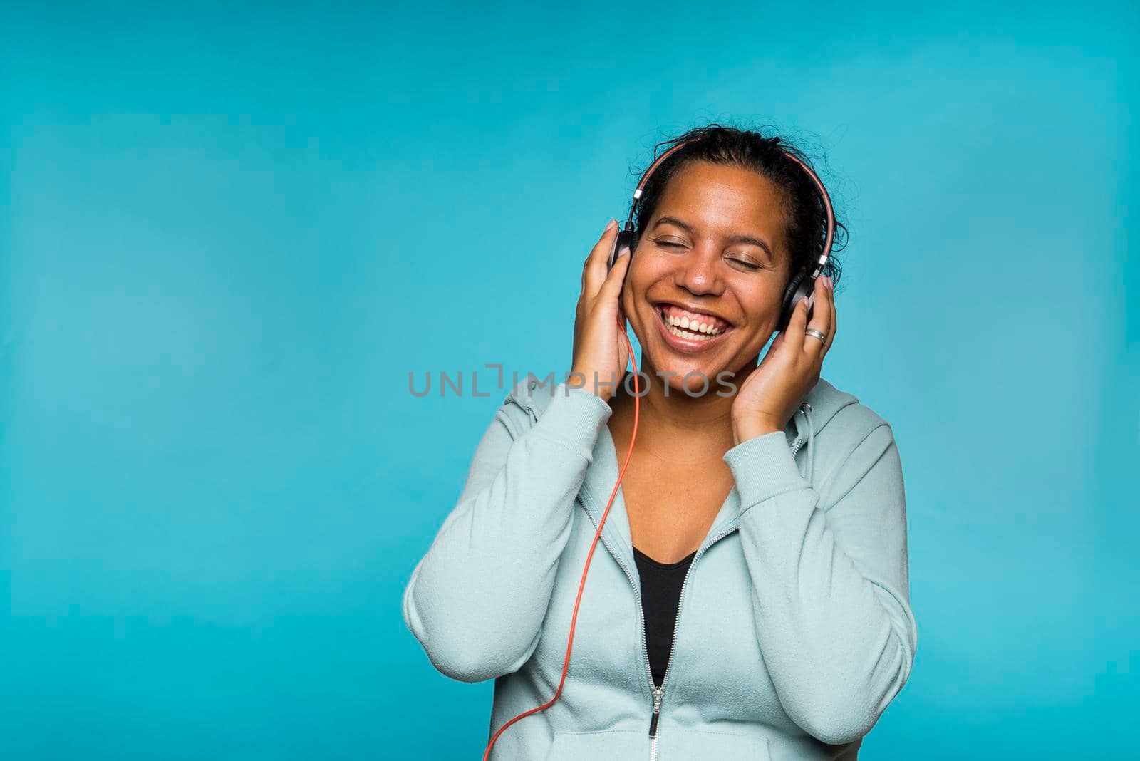 Young attractive mixed race woman enjoying music listening with headphones blue background by LeoniekvanderVliet