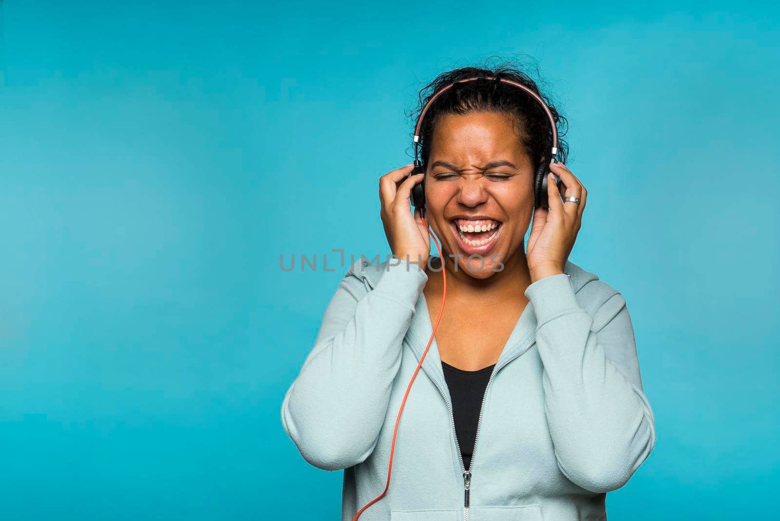 Young attractive mixed race woman enjoying music listening with headphones blue background by LeoniekvanderVliet