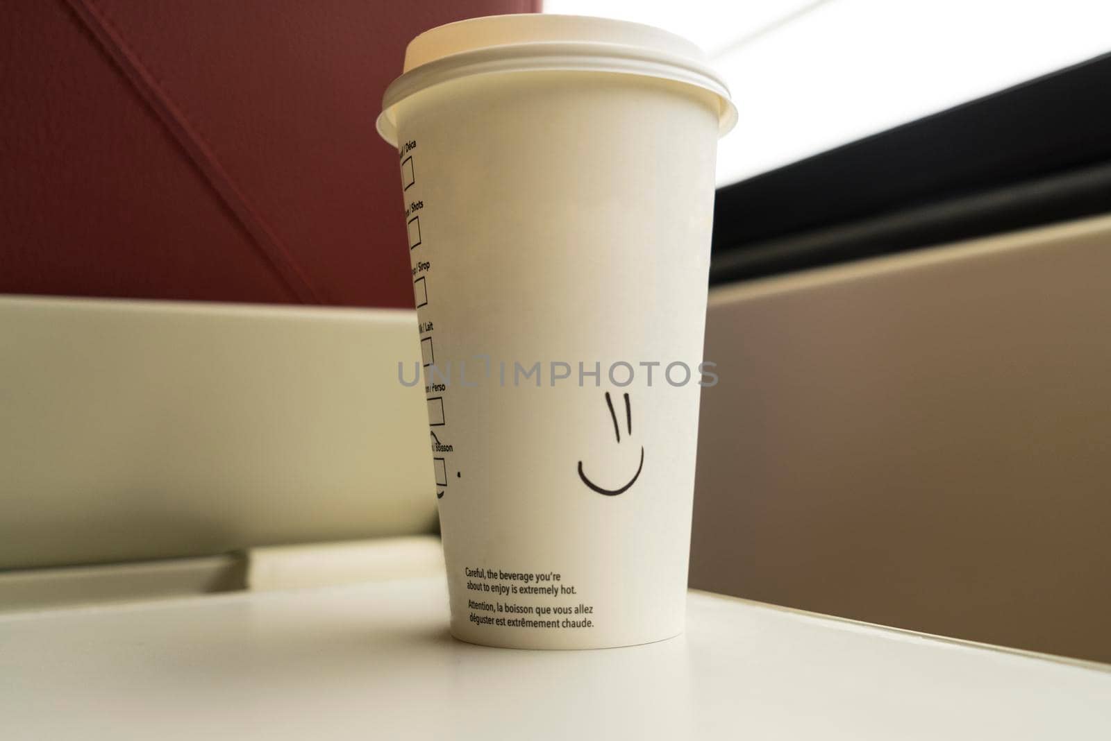 Disposable coffee cup with a smiley drawn on it standing on a table in a train