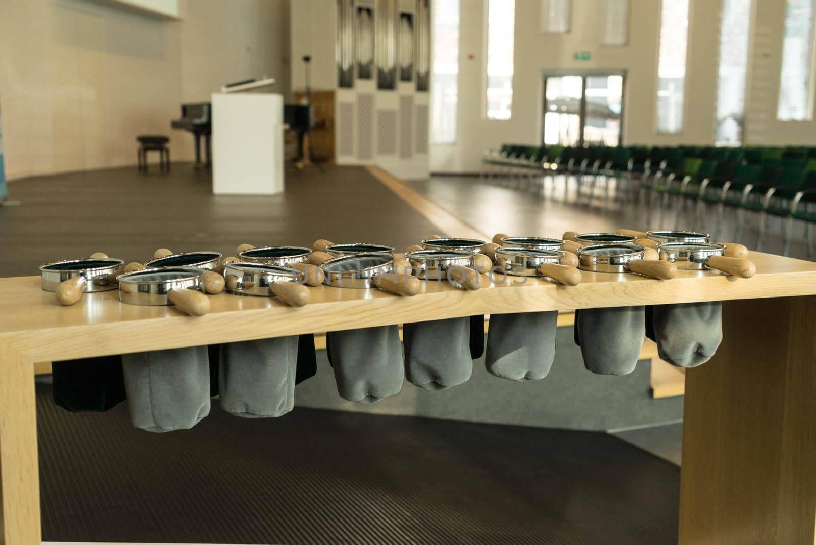 Rack with grey velvet offering or collecting bags in a church with chairs and the altar behind them by LeoniekvanderVliet