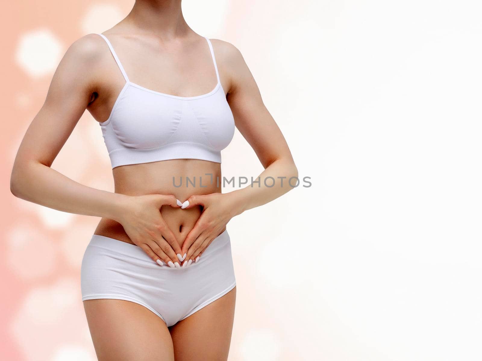 Slim woman in white underwear forming a heart symbol with her hands on her belly against an abstract background with circles and copyspace