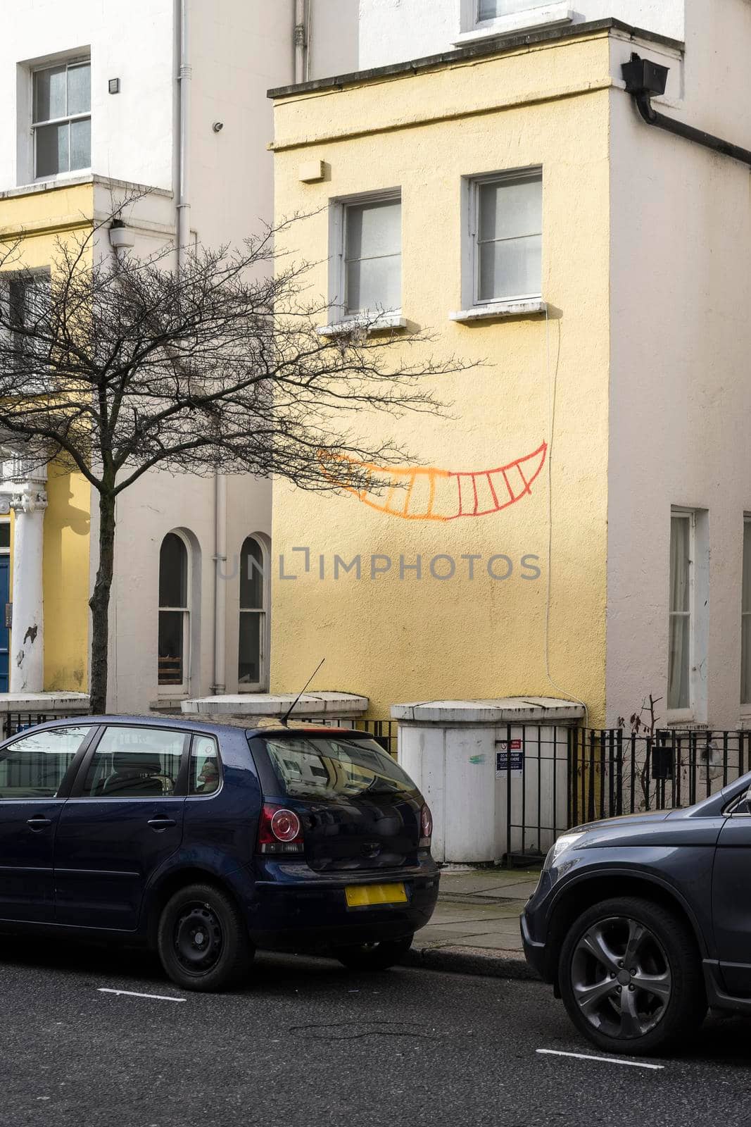 Yellow building with two windows and a smile drawn on the wall resembling a smiling face in Chelsea London England by LeoniekvanderVliet