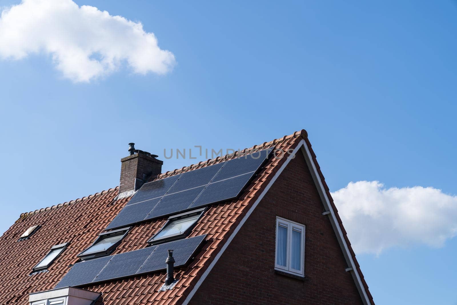 Roof with red roof tiles and solar panels for making renewable energy and a clear blue sky by LeoniekvanderVliet