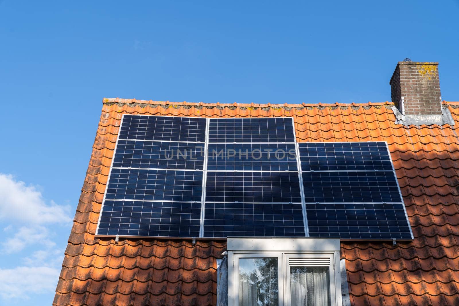 Roof with red roof tiles and solar panels for making renewable energy and a clear blue sky by LeoniekvanderVliet