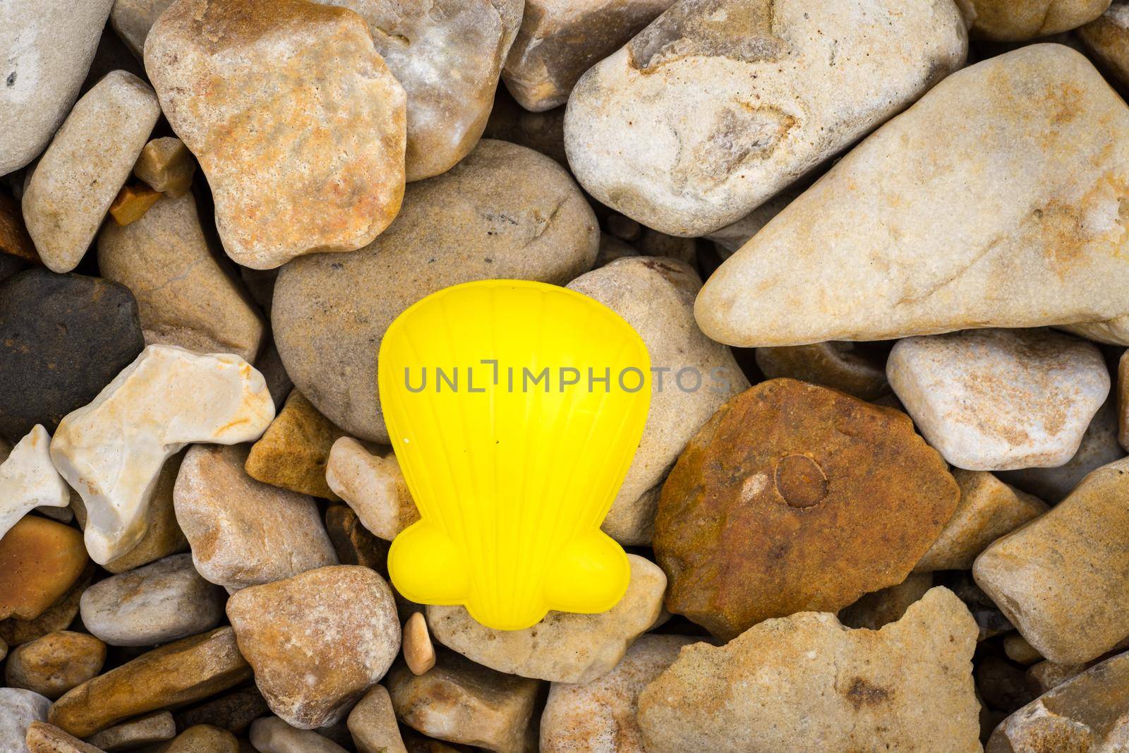 A sand mold in the shape of a shell, yellow, lying on a pebble beach in the South of England