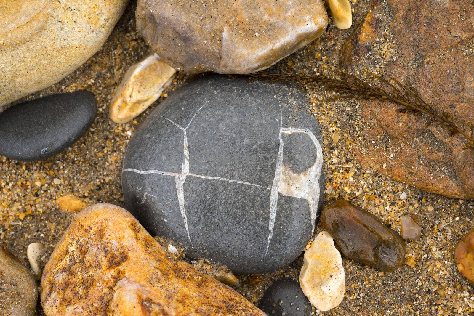 A close up of grey and yellow pebbles with chrystal lines lying on a sandy beach in the South of the United Kingdom