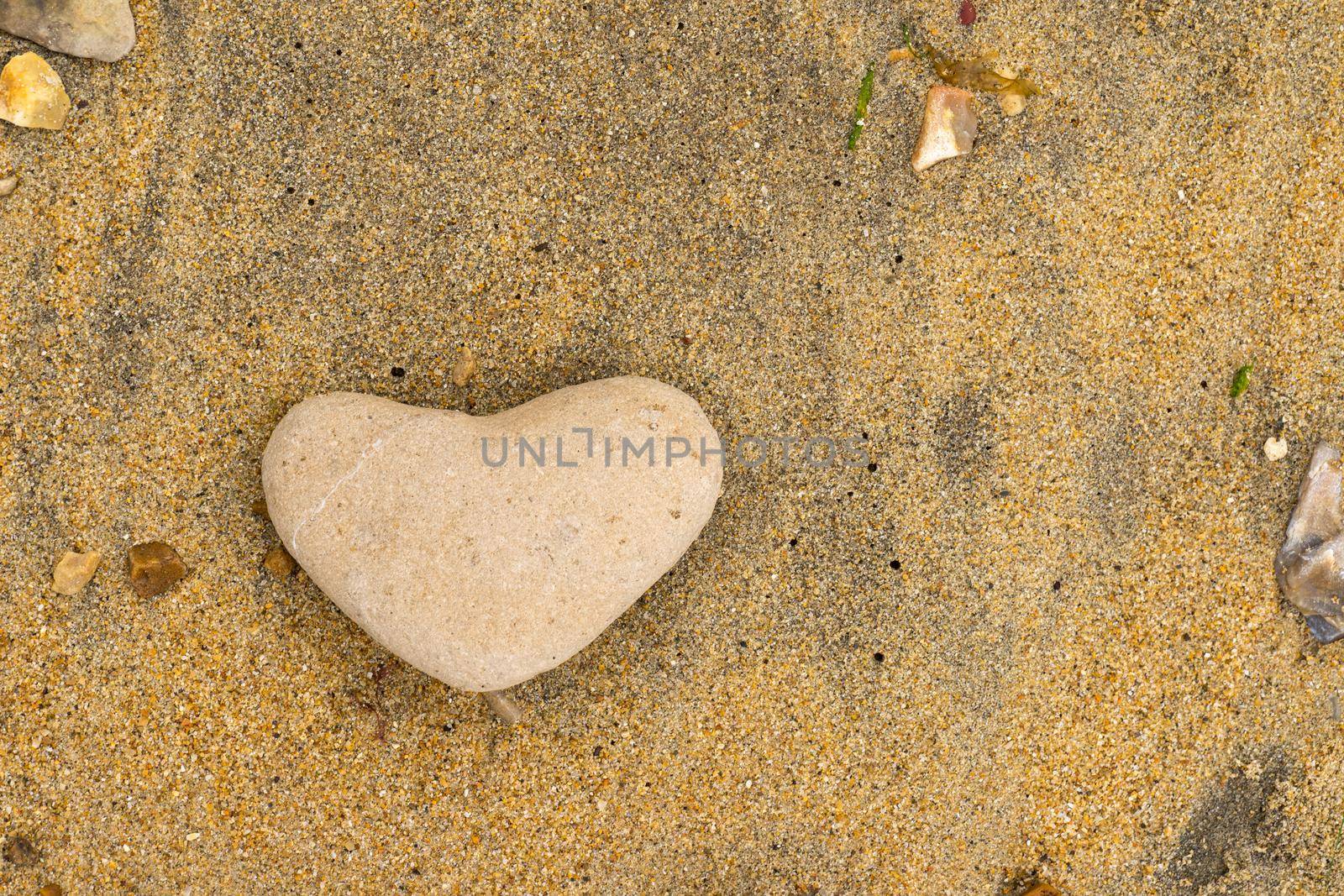 A close up of a yellow heartshaped pebble lying on a sandy beach in the South of the United Kingdom