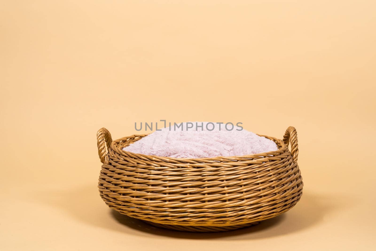 A close up of an empty basket with a pink cushion against a beige creme background