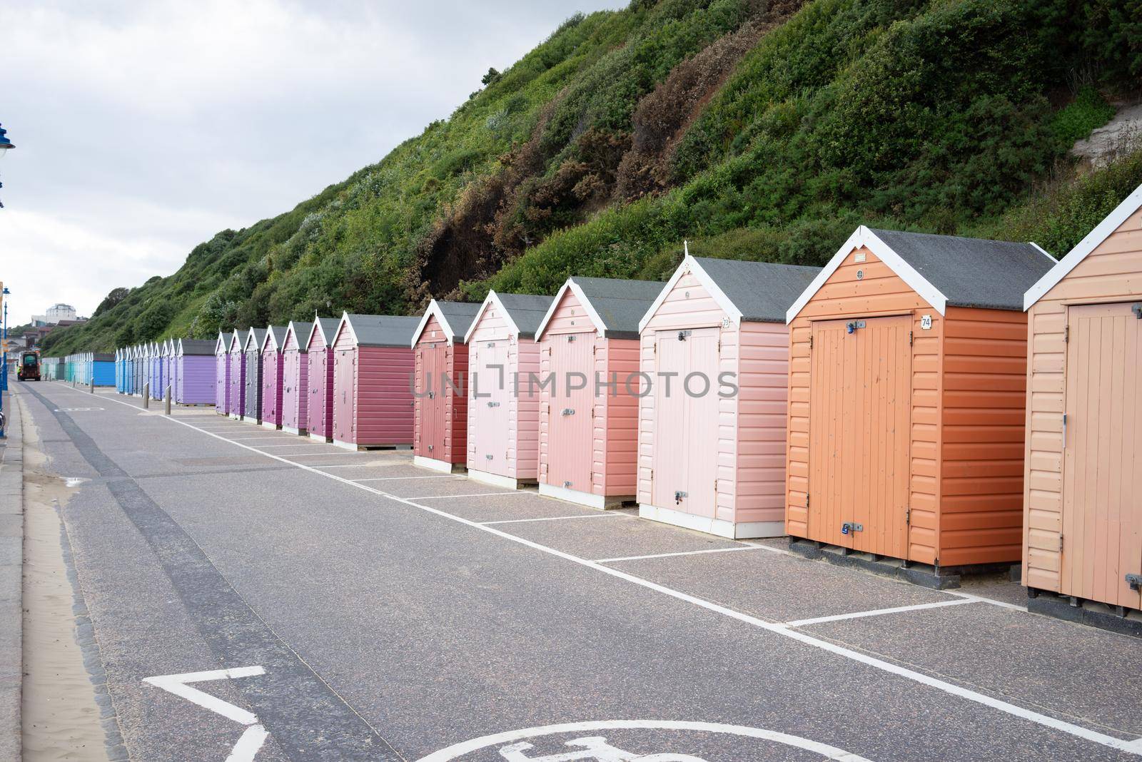 Colorful Beach huts, in orange, peach and pink colors, at the  boulevard in Bournemouth, Dorset, UK, England on a cloudy day in summer by LeoniekvanderVliet