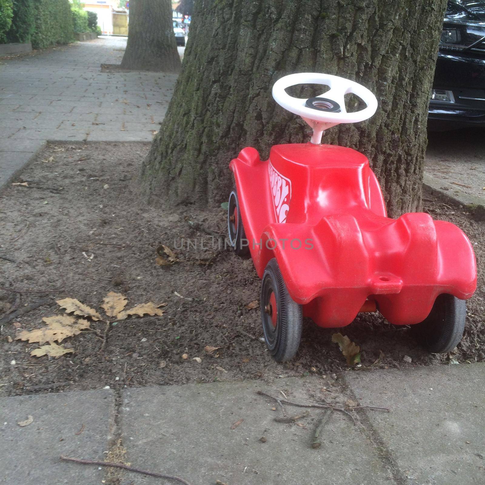 a Little red toy car parked against a tree in a street
