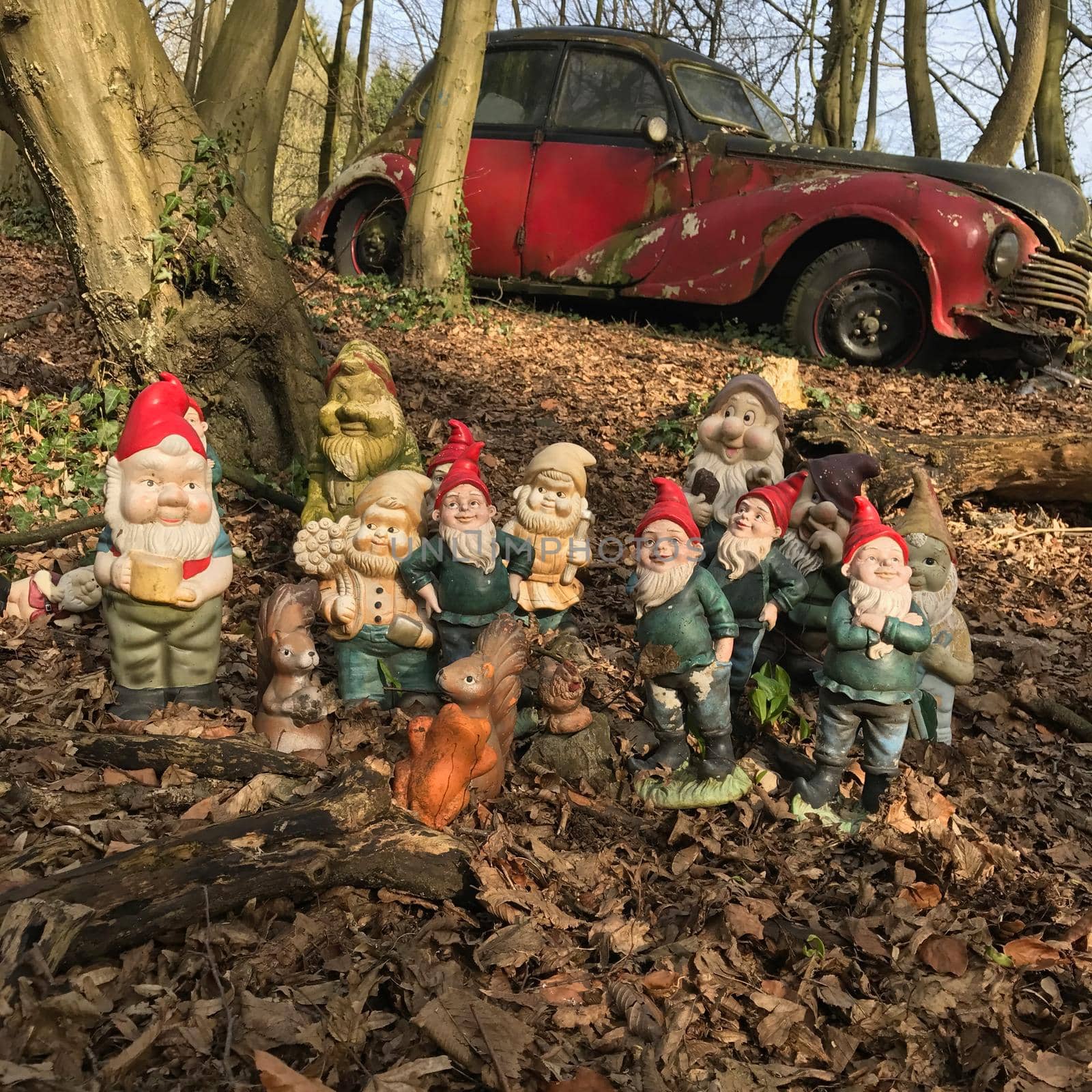 Group of stone gnome statues in an autumn forest with a old abandoned car in the background by LeoniekvanderVliet