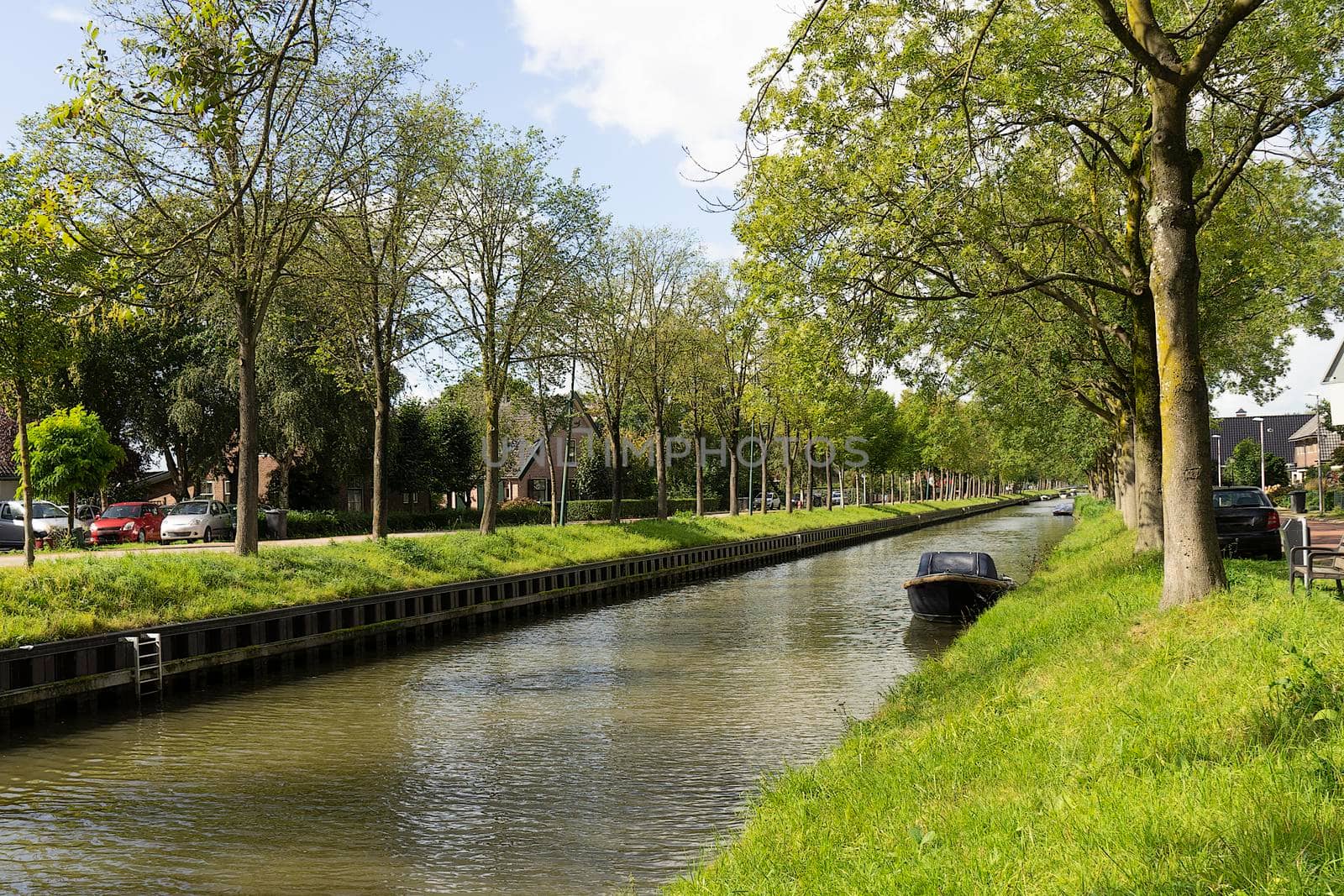 The canal of The Leidsche Rijn in De Meern, near Utrecht The Netherlands on a sunny spring day with trees and boat by LeoniekvanderVliet