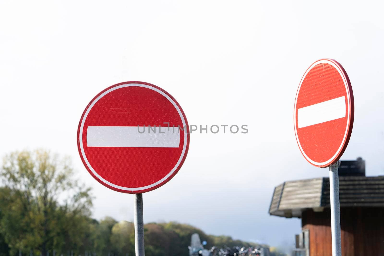 Two red circular traffic signs or roadsign with a white bar indicating no entry on a grey metal post against a cloudy sky in a forest area by LeoniekvanderVliet