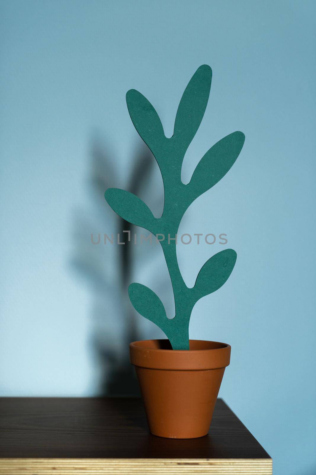 An artificial wooden plant shape in a terracotta pot on a wooden table on a blue background. The concept of office interior, home comfort, lifestyle. Mock-up with copy space for your text.