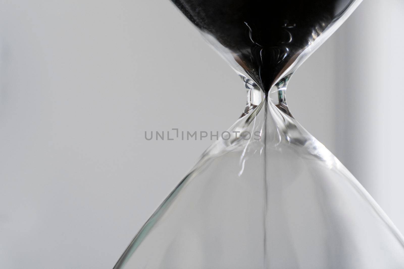 Black sand running through the bulbs of an hourglass measuring the passing time in a countdown to a business deadline, urgency and running out of time on a light background with copy space close up by LeoniekvanderVliet