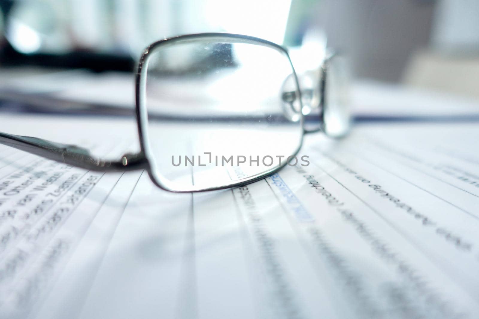 A close up of eye glasses lying on an office table with unrecognisable paper and documents selective focus ans space for tekst or copy