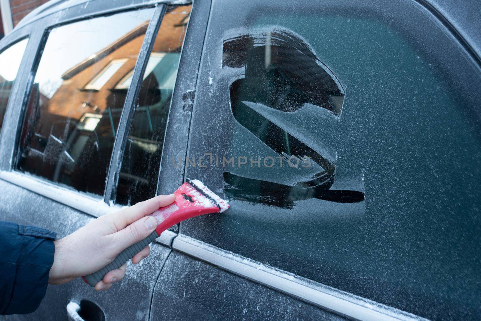 Cleaning the side car windows of snow with ice scraper before the trip. Man removes ice from car windows. A male hand.