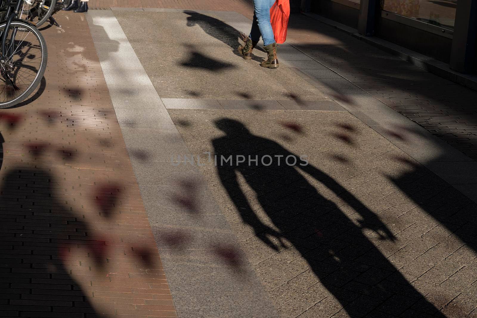 Shadow of a man following a woman on the pavement looking suspicious or scary, concept for an assault or attack by LeoniekvanderVliet