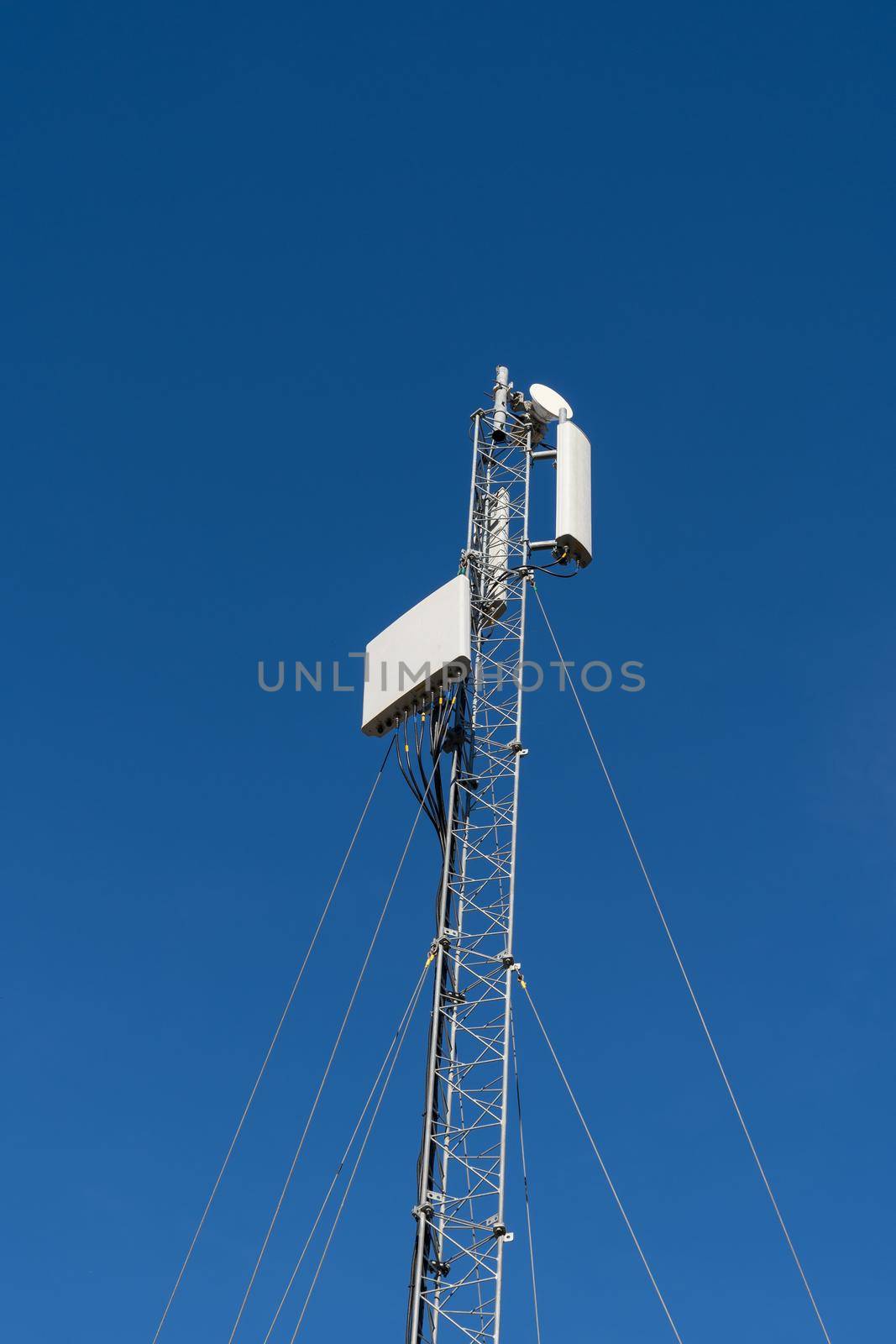 Modern wireless telecommunication tower antenna transmitter or base reciever station for broadcasting 4G or 5G cellular telephone, television, and Internet signals, against a blue sky. by LeoniekvanderVliet