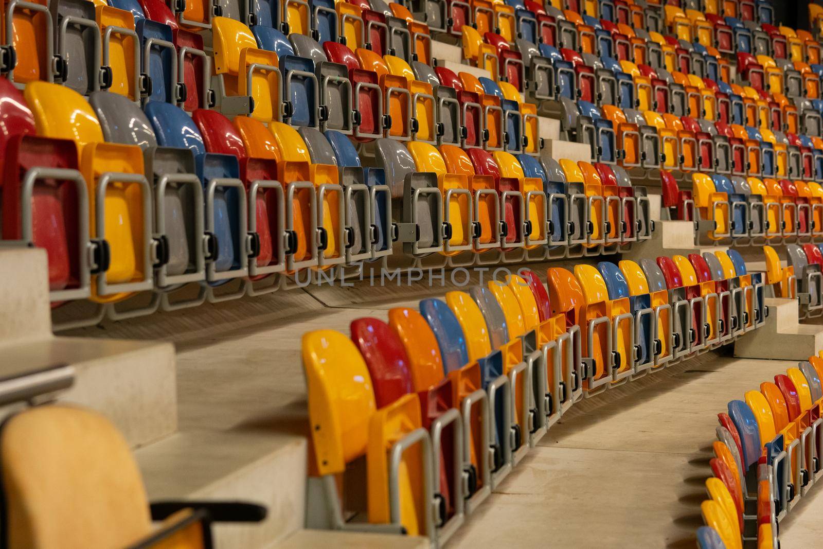Rows of folded, green, blue, yellow, green and orange plastic seats in a very big, empty indoor stadium
