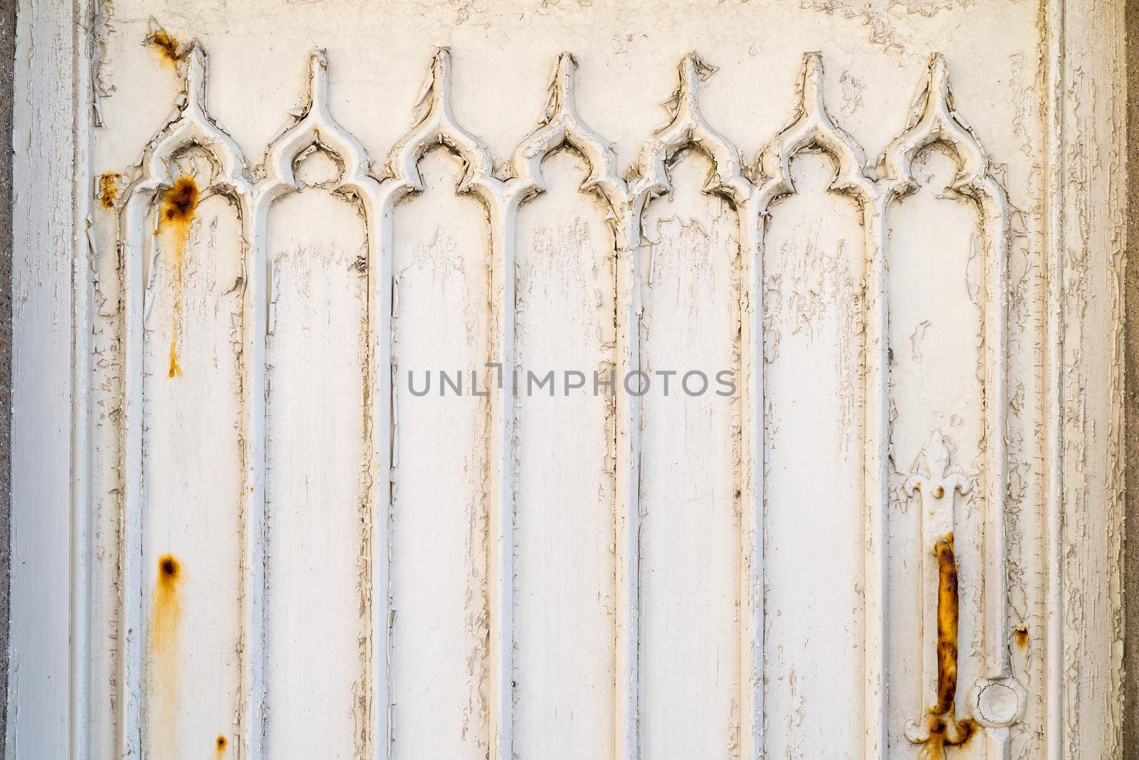 a Detail of a white wooden door with weathered and rusty paint and gothic window pattern relief