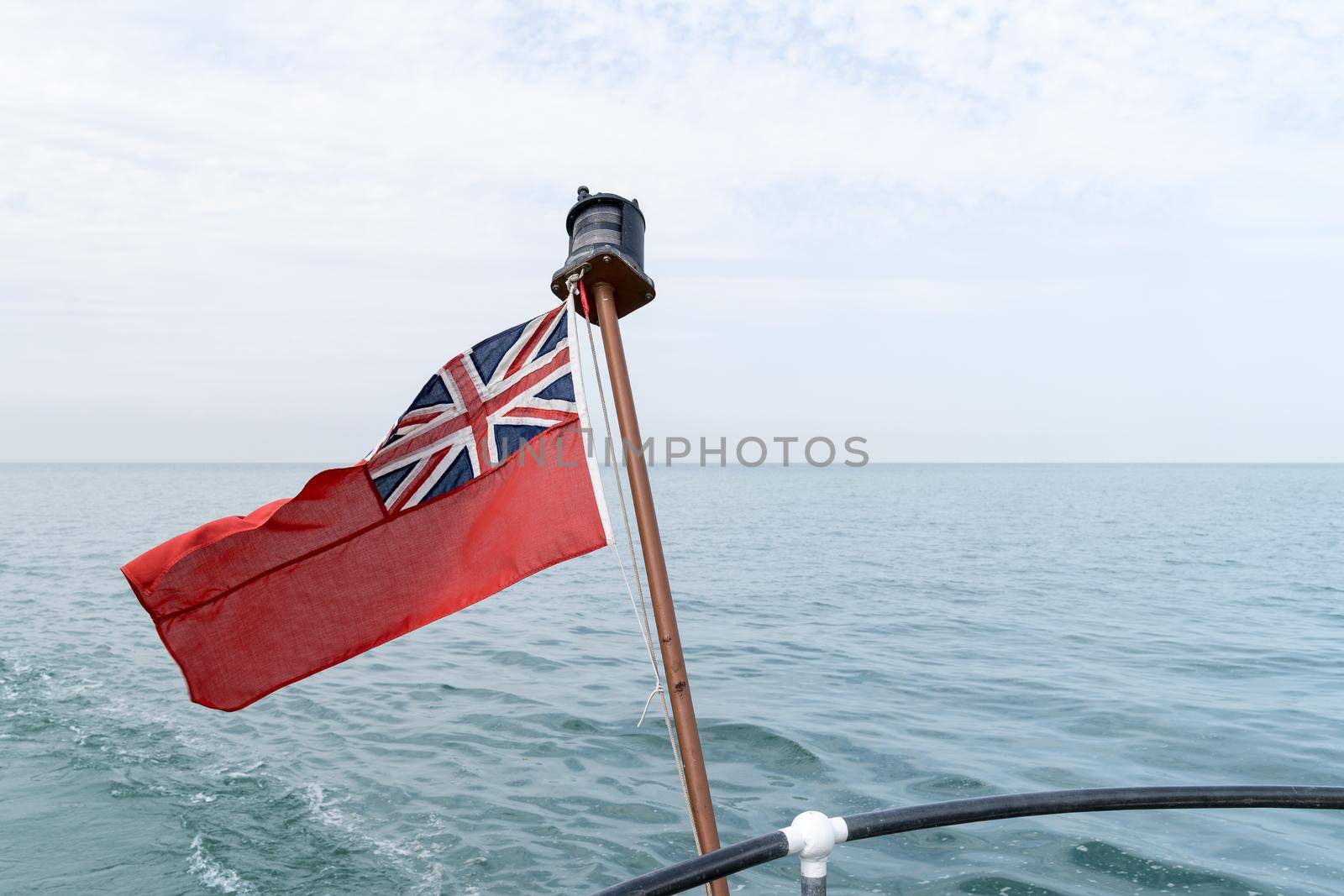 an Uk red ensign the british maritime flag flown from yacht with the sea and sky behind it