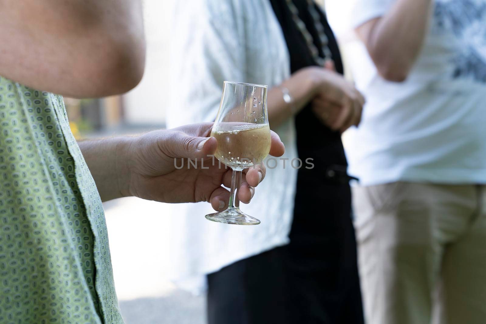 Male hands holding a glass of white wine at an outdoor wine tasting