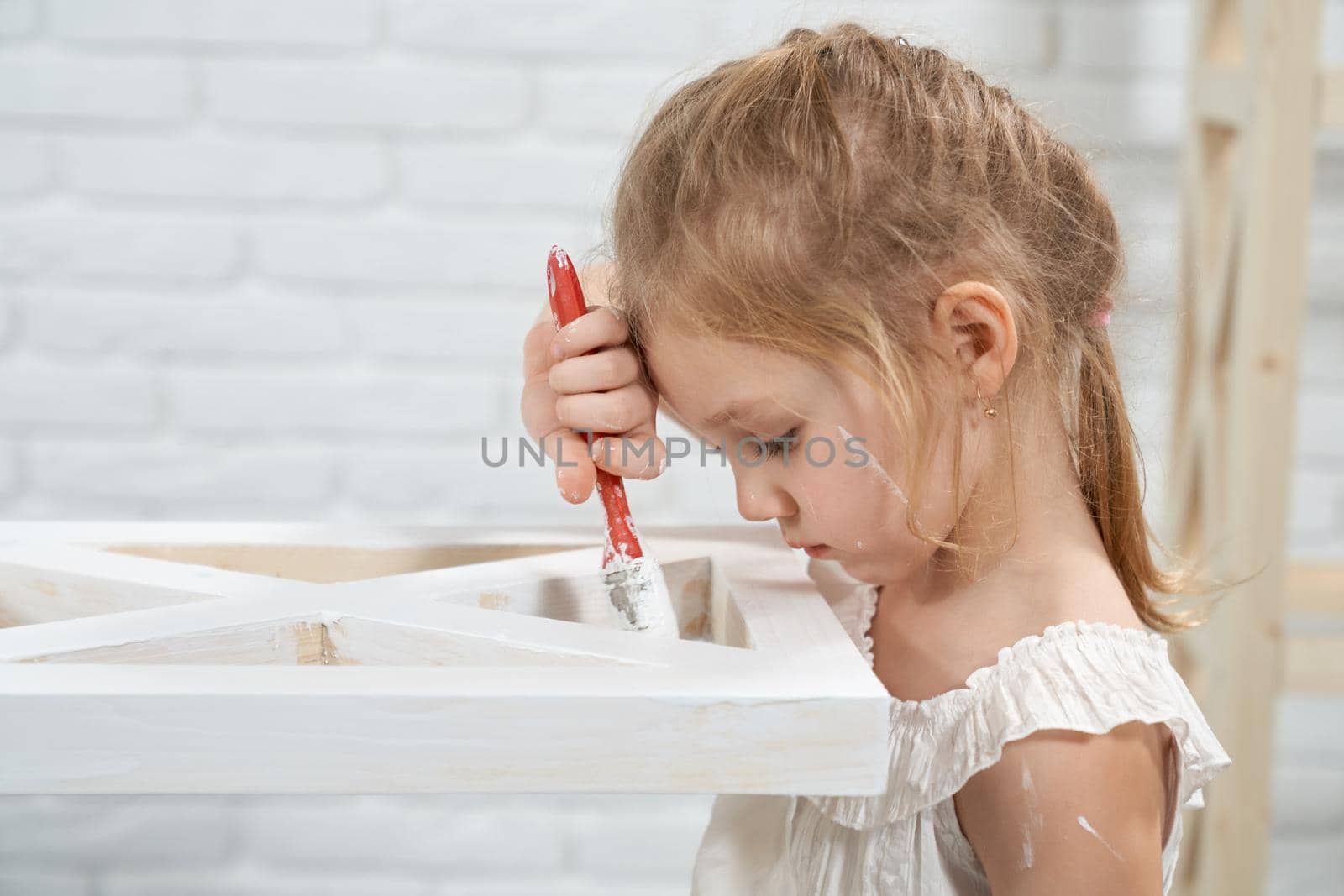 Concept of cute little girl painting with brush wooden rack in white color at home. Concept of improvement rack.